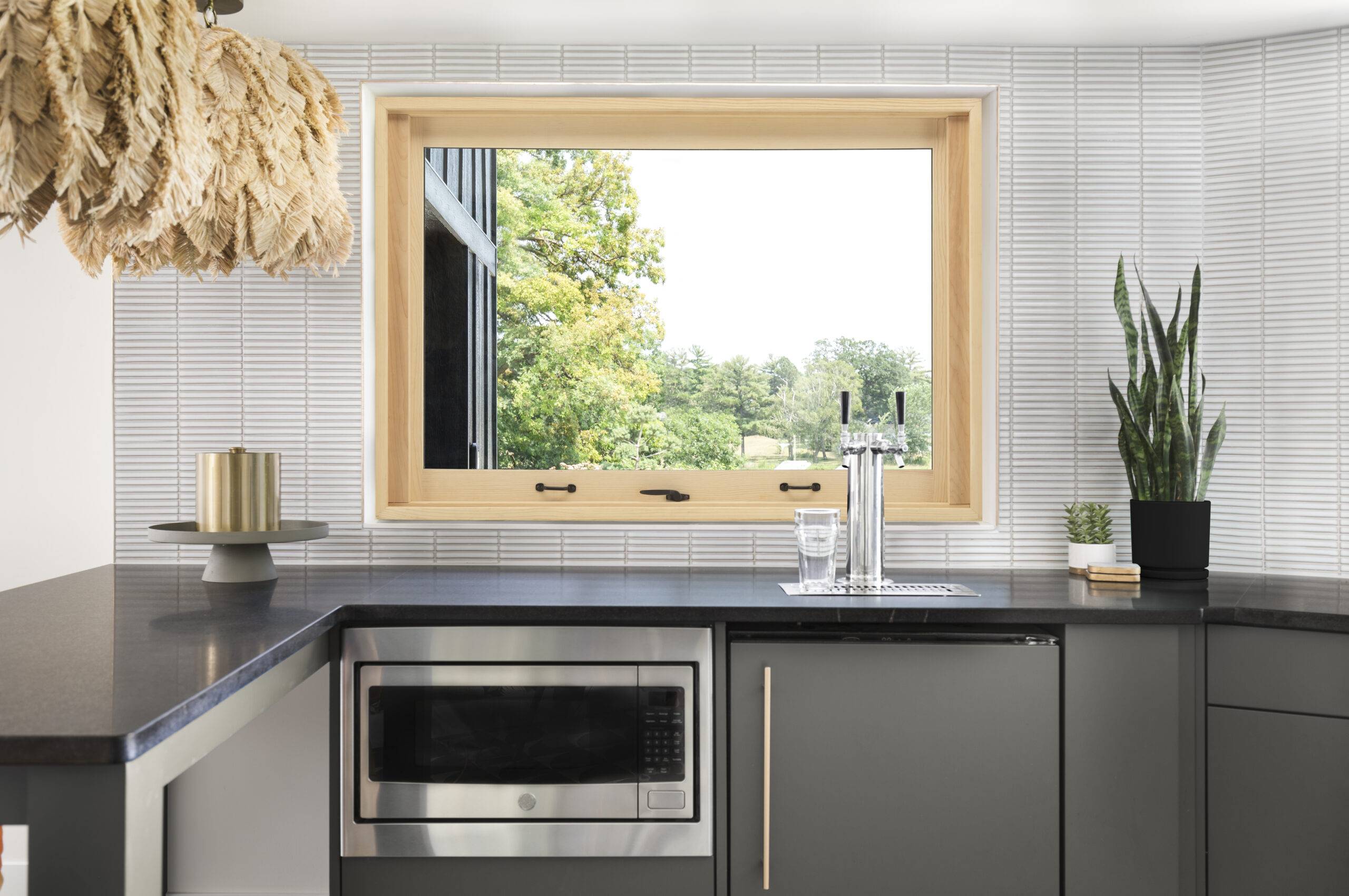 Kitchen with stainless steel appliances, black granite countertops, and a large light wood trim Marvin Signature Ultimate window.