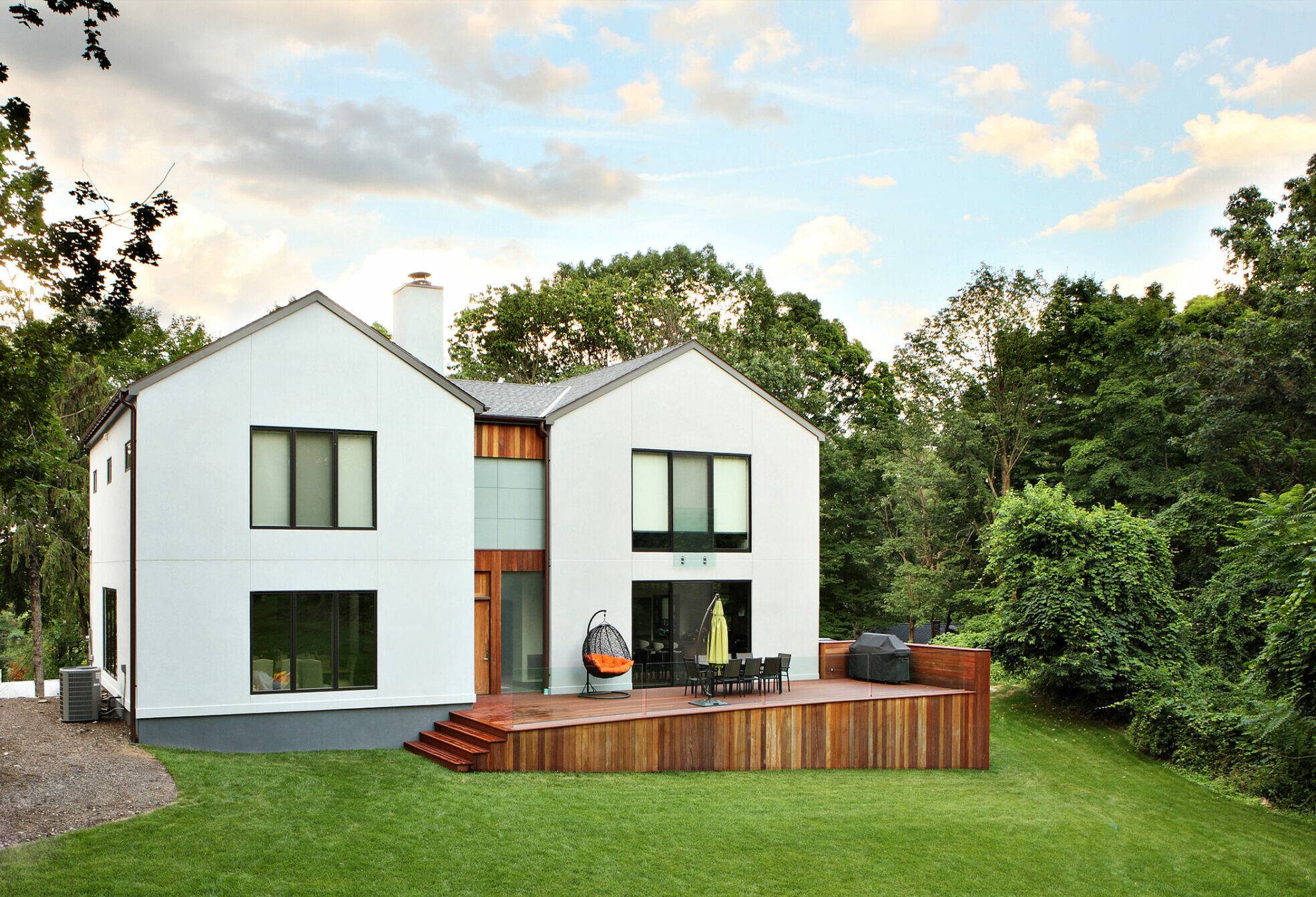 A white modern home with a rustic wood deck and large yard.